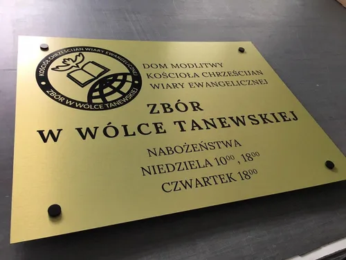 Tablica ze złotej płyty alubond z czarnymi napisami i czarnymi dystansami, widok z przodu.