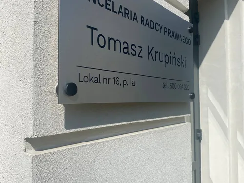 Tabliczka kancelarii radcy prawnego z ciemnymi napisami i czarnymi dystansami na elewacji.