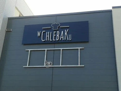 Logo W Chlebaku na ciemnym panelu elewacyjnym