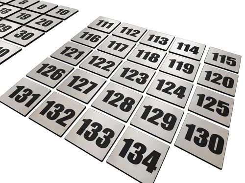 Srebrne tabliczki z laminatu z dużymi czarnymi numerami od 111 do 134, ułożone w rzędach, oraz fragment dodatkowej serii numerów.