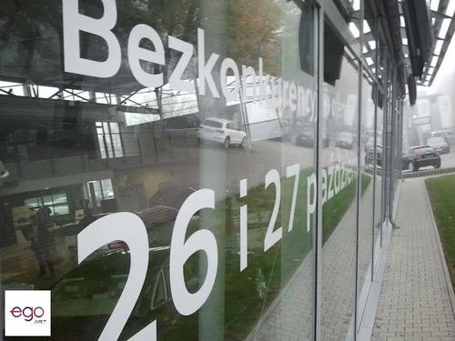 Białe napisy promocyjne na witrynie salonu samochodowego